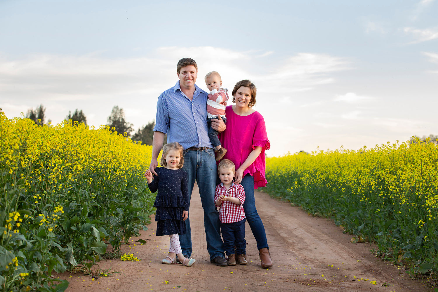 Family of five standing on a dirt road in a paddock of canola flowers