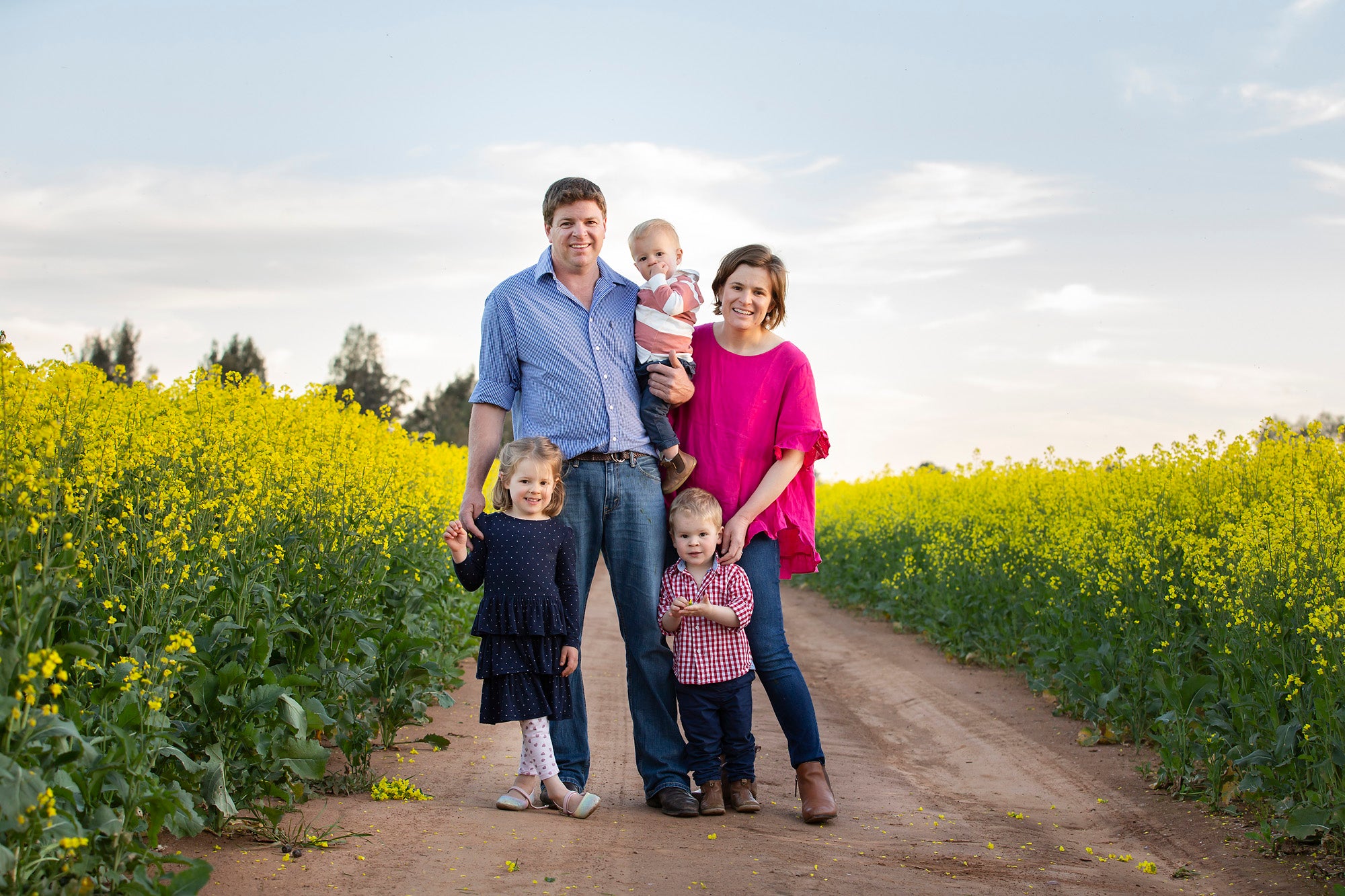 Family of five standing on a dirt road in a paddock of canola flowers