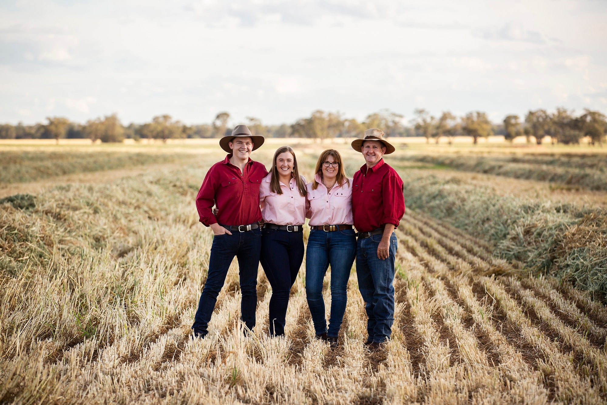 Four people standing in a field wearing red shirts and hats.